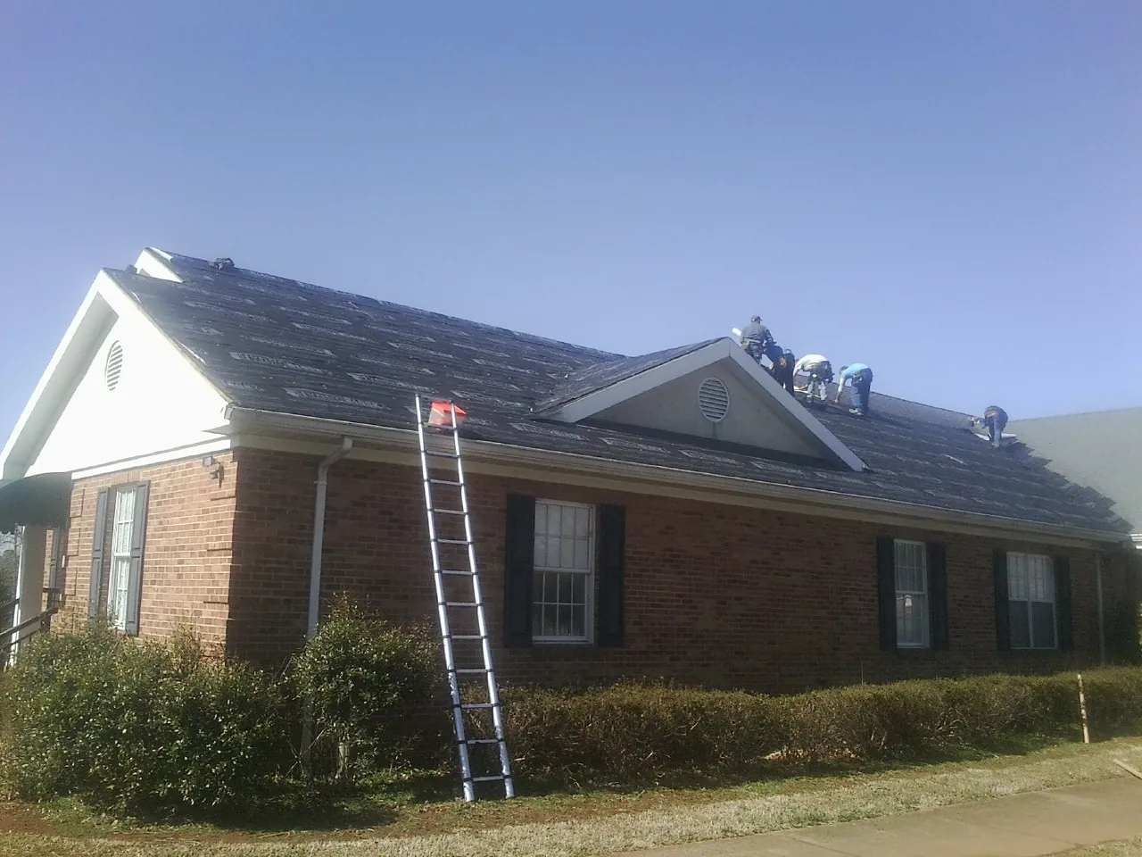 Crew tearing shingles off a brick ranch roof with a ladder set — Emergency Roof Repair work by our crew in Hobe Sound
