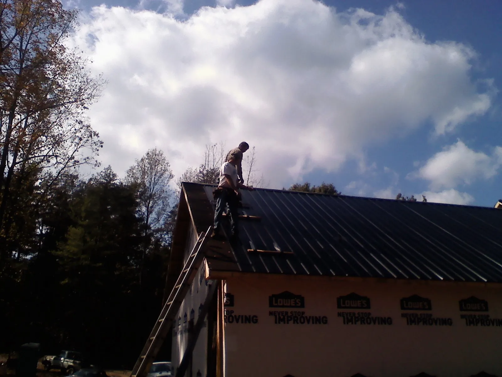 Roofer fastening dark metal panels high against a cloudy sky, from a Roof Inspection job in Hobe Sound