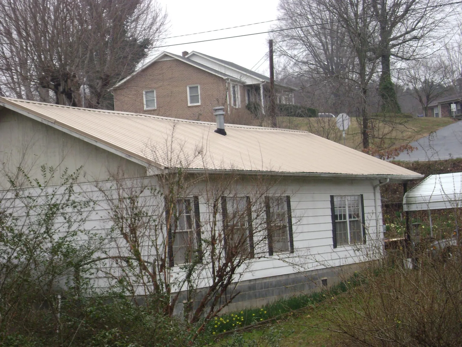Tan metal roof on a white sided house set into a hillside — Commercial Roofing by Roofing Brothers in Hobe Sound